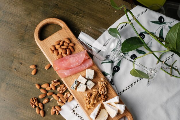 Tablero de madera con nueces queso y jamón y copa de vino