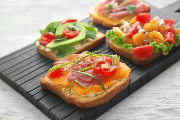 Tablero de madera con sabrosos sándwiches en la mesa