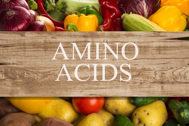 Tablero de madera con texto AMINO ACIDS entre diferentes productos y verduras