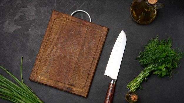 Tablero de madera vacío cebollas verdes manojo de eneldo y perejil en una vista superior de la mesa negra