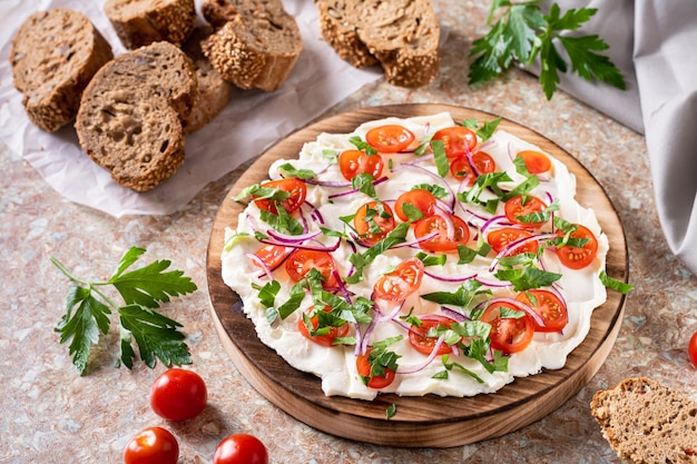 Tablero de mantequilla de moda con tomates, cebollas y perejil y rebanadas de pan sobre la mesa