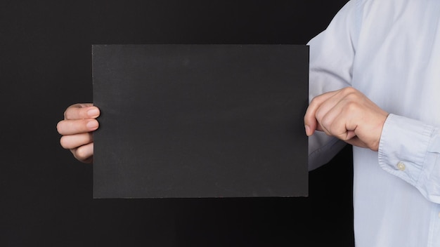 Tablero negro en blanco Papel A4 en la cara cubierta de la mano del hombre y camisa azul sobre fondo negro x9