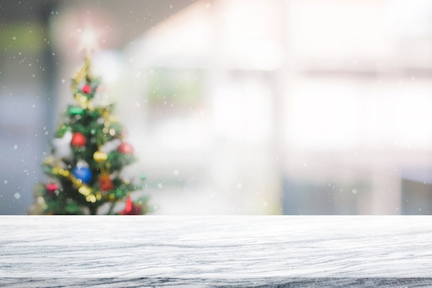 Tablero de piedra de mármol blanco en la falta de definición con el fondo del árbol de navidad del bokeh con las nevadas - se puede utilizar para la exhibición o el montaje de sus productos