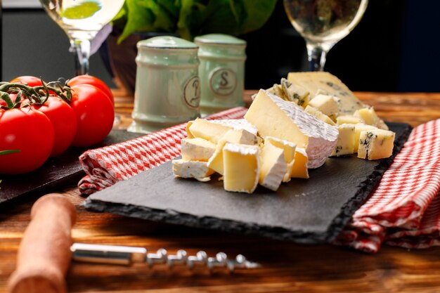 Tablero de piedra con queso cortado en la mesa de madera de cerca