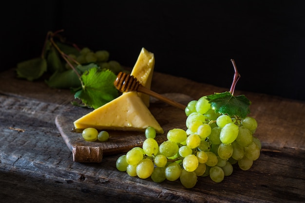 Tablero de pizarra con queso. Queso y uvas en madera con miel. Concepto de desayuno. Bodegón