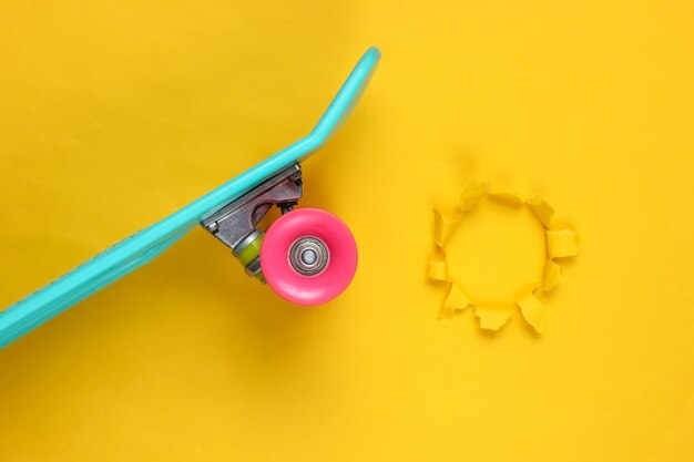 Foto tablero de plástico mini cruiser sobre fondo amarillo con agujero rasgado. tendencia de color pastel. verano divertido. concepto minimalista juvenil.