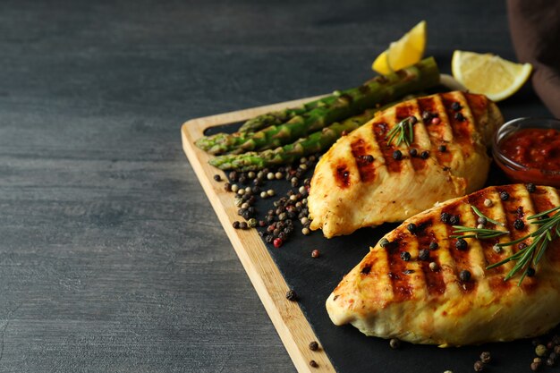 Tablero con pollo a la parrilla e ingredientes en madera oscura.