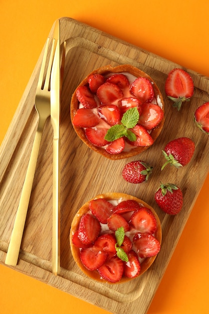 Tablero con tartas de fresa sobre fondo naranja.