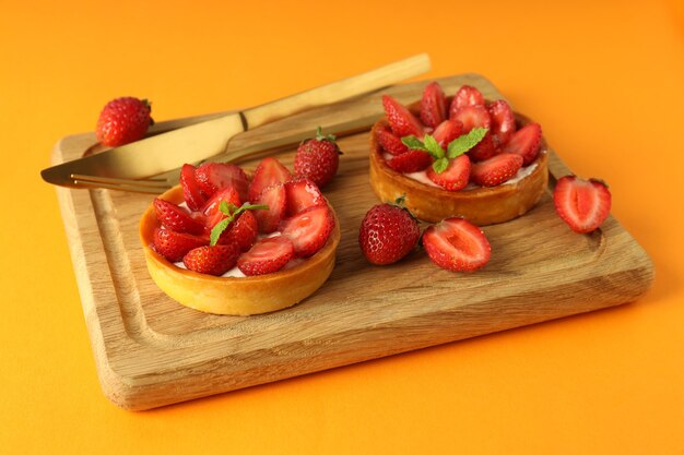 Tablero con tartas de fresa sobre fondo naranja.