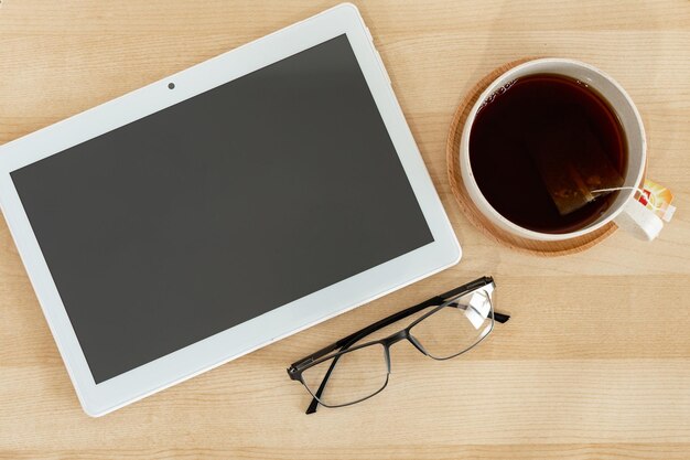 Tablet anteojos y taza de té en el escritorio de oficina de madera