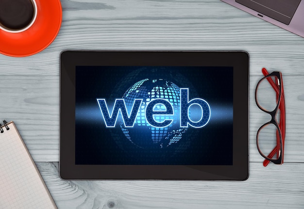 Tablet-Anzeigeweb mit digitalem Globus auf dem Schreibtisch mit Kaffee-Notebook-Gläsern