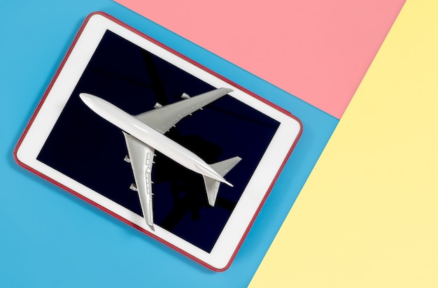 Tablet com avião para o conceito de viagens na rosa amarela azul