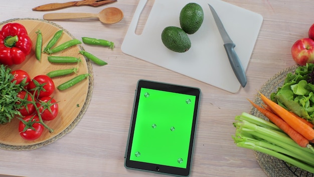 Tablet com tela verde na cozinha na mesa com legumes frescos e frutas Aplicativo para cozinhar Conceito de comida saudável