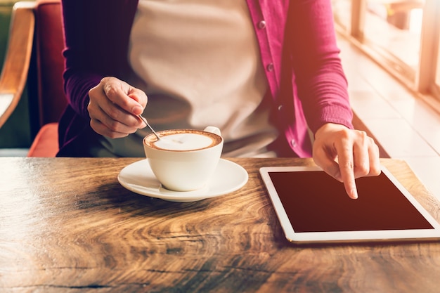 Tablet-Computer und Schale der Handfrauen-mit Berührungseingabe Bildschirm in der Kaffeestube mit Weinleseton.