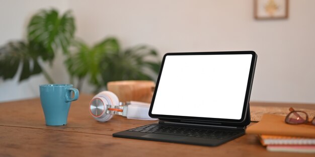 Tablet de computador de tela em branco com uma caixa de teclado está colocando sobre uma mesa de trabalho de madeira.