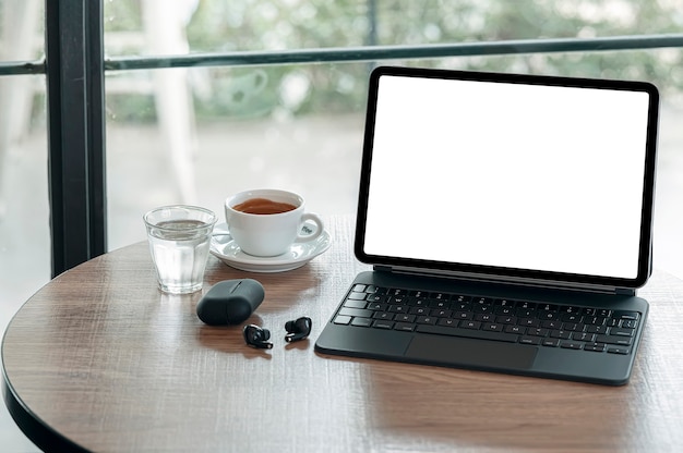 Tablet de tela em branco com teclado e café na mesa redonda de madeira no café.