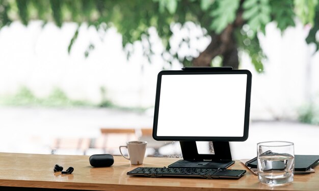 Tablet de tela em branco de maquete com suporte de suporte e teclado na mesa de balcão de madeira no café.