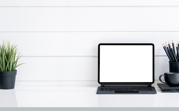 Tablet de tela em branco de maquete com teclado mágico e suprimentos na mesa branca, conceito de espaço de trabalho preto e branco.