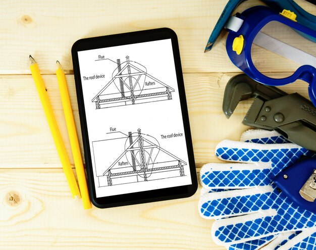 Tablet, desenhos e ferramentas de trabalho em uma mesa de madeira.