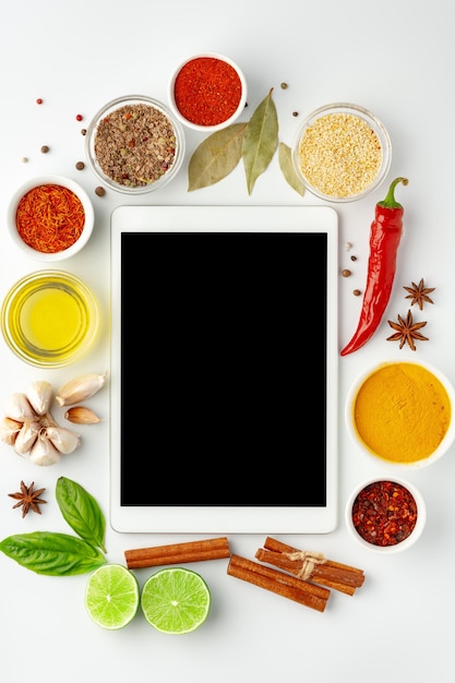 Foto tablet digital cercado por ingredientes de culinária e especiarias em fundo branco vista de cima