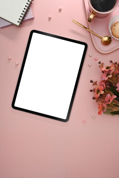 Tablet digital com notebook de xícara de café de tela em branco e flor vermelha em fundo rosa