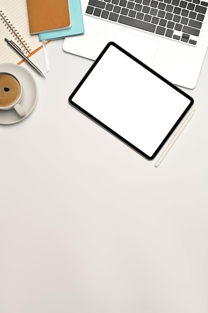 Tablet digital de vista superior com notebook de tela vazia e xícara de café na mesa branca