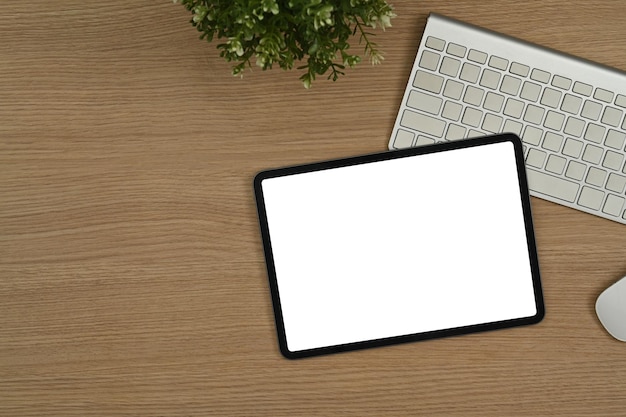 Tablet digital esfolado com teclado de exibição vazio branco e planta em vaso na mesa de madeira