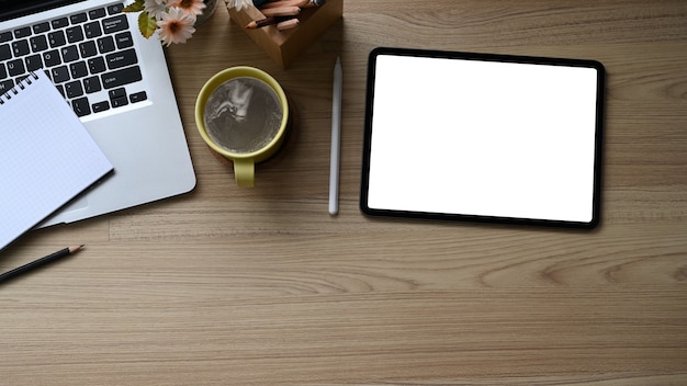 Tablet digital, laptop e xícara de café na mesa de madeira.