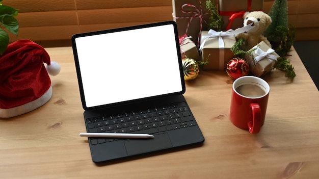 Tablet digital, xícara de café e caixas de presente de Natal na mesa de madeira.