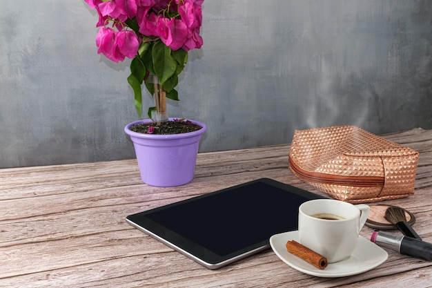 Tablet em cima da mesa cercado por batom de xícara de café e visão de bolsa de maquiagem