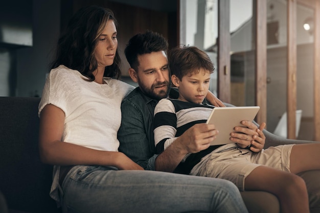 Tablet familia y padres con niño en el sofá para el aprendizaje educación y vinculación tecnología digital madre y padre con niño en la sala de estar de la casa para la transmisión de películas video y ver dibujos animados