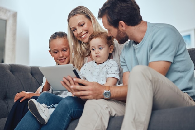 Tablet familiar feliz e sofá relaxado na sala de estar juntos para momentos de qualidade e streaming de vídeo on-line pais filhos sorriem e assistem no dispositivo de tecnologia digital no sofá na casa da família