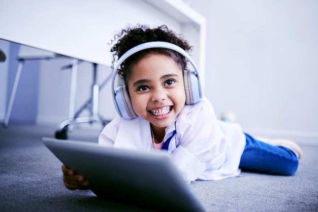 Tablet-Kopfhörer und Bildung mit einer Studentin, die zu Hause auf dem Boden liegt, um im virtuellen Fernunterricht Technologie zu lernen, und lächeln, während eine glückliche junge Schülerin sich ein Schulvideo ansieht