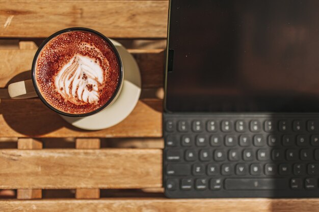 Tablet mit heißem Kaffee auf dem Schreibtisch mit warmer Sommersonne