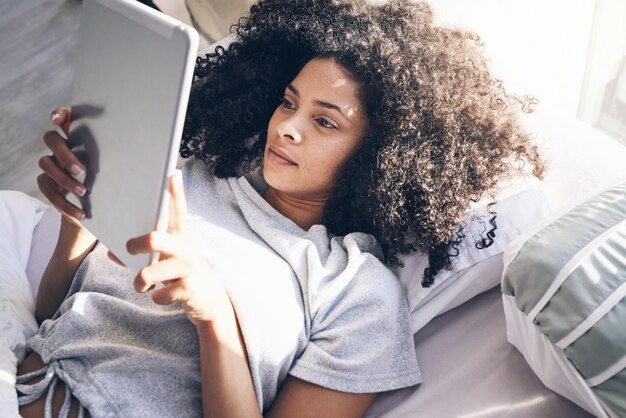 Foto tablet mulher negra e relaxe na cama no quarto para mensagens de texto de mídia social ou navegação na internet pela manhã tecnologia doméstica e feminina com tela sensível ao toque digital para rolagem na web depois de acordar