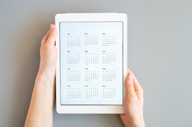 Tablet PC con una aplicación abierta de calendario para un año de fecha desconocido no especificado sin fecha en manos de una mujer en un negocio de concepto de fondo gris o para hacer una lista de objetivos vista superior plana
