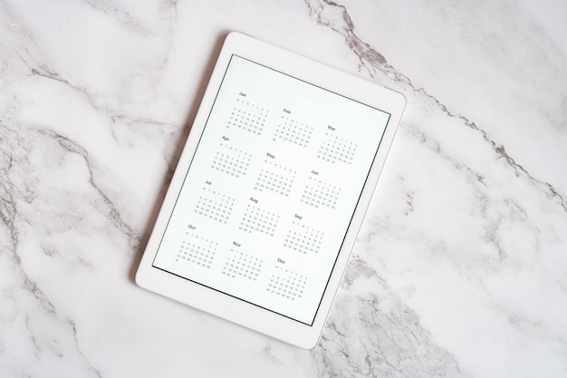 Tablet PC con una aplicación abierta de calendario para un año de fecha desconocido no especificado sin fecha en un negocio de concepto de fondo de mármol gris o para hacer una lista de objetivos con tecnología usando vista superior plana