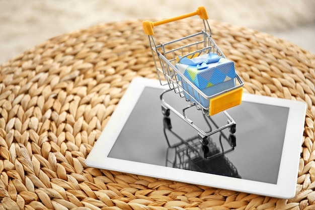 Tablet PC y carrito de compras pequeño con caja de regalo en puf de mimbre Concepto de compras por Internet