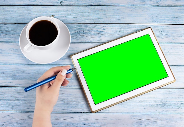 Tablet PC com tela verde perto de uma xícara de café em uma mão de fundo de madeira com uma caneta