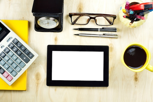 Tablet-PC mit leerem Bildschirm und einem Tasse Kaffee, Finanzrechner auf gelbem Notizbuch