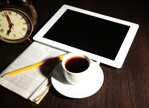 Tablet periódico taza de café y despertador en mesa de madera