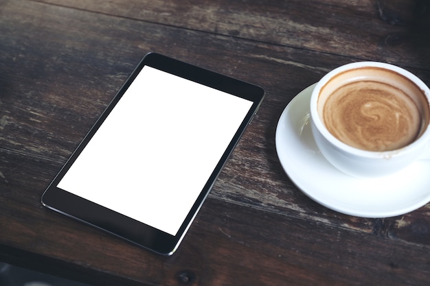 tablet preto com tela de desktop em branco branco e xícara de café na mesa de madeira vintage