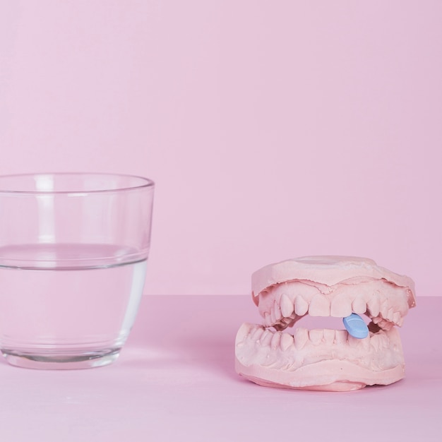 Tableta azul dentro del molde de yeso modelo dental con vaso de agua sobre fondo rosa