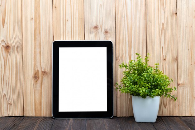 Tableta en blanco y pequeño árbol sobre fondo de madera