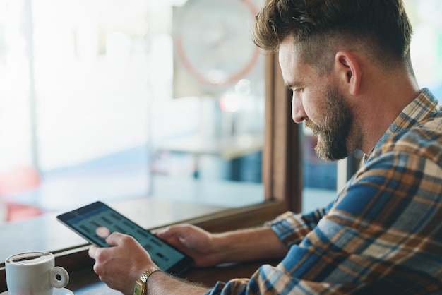 Tableta de cafetería y hombre con bebida junto a la ventana para trabajo remoto compras en línea y redes restaurante freelance y persona en tecnología digital en el café para investigación y propuesta de noticias en Internet