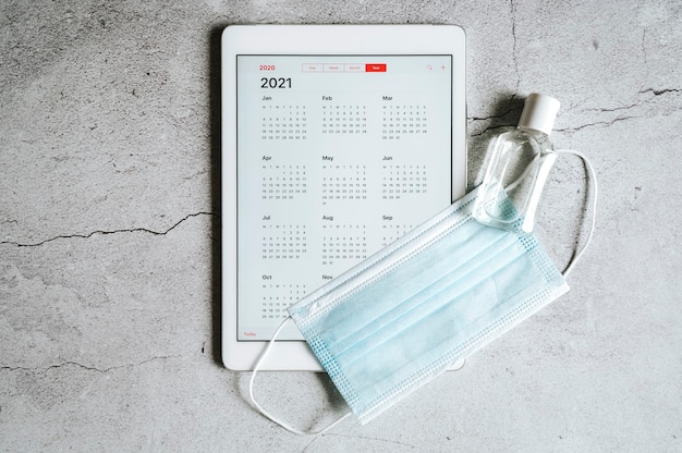 Foto una tableta con un calendario abierto para el año 2021 y una máscara médica protectora.