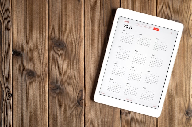 Una tableta con un calendario abierto para el año 2021 sobre un fondo de mesa de tablas de madera. espacio para texto