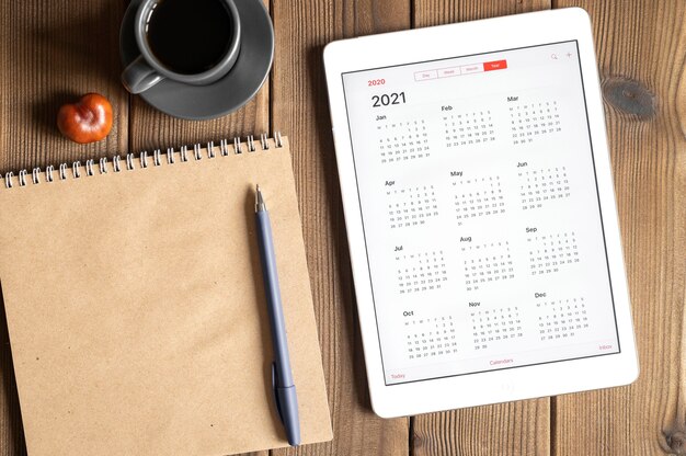 Foto una tableta con un calendario abierto para el año 2021, una taza de café, castañas y un cuaderno de papel artesanal sobre un fondo de mesa de tablas de madera