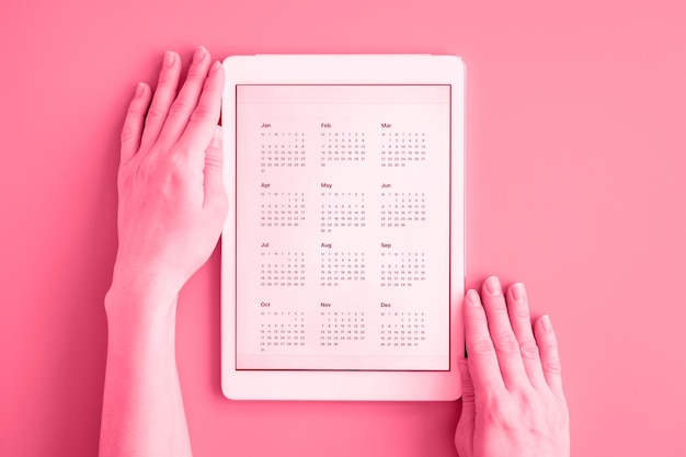 Tableta con calendario de aplicación para fecha desconocida no especificada año sin fecha en manos de mujeres negocio o para hacer lista de objetivos vista superior plana tonificada en viva magenta color de tendencia del año 2023