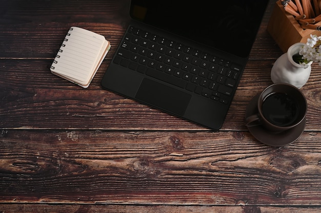 Tableta de computadora, cuaderno y taza de café en la mesa de madera.